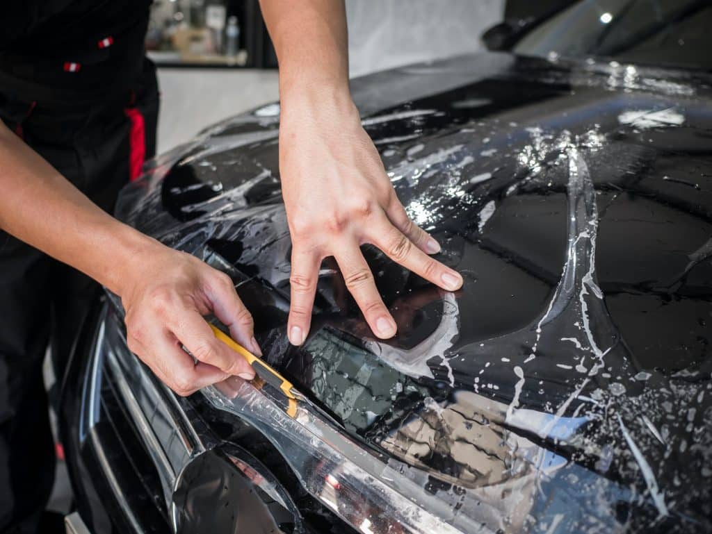 Hands installs car paint protection film.
